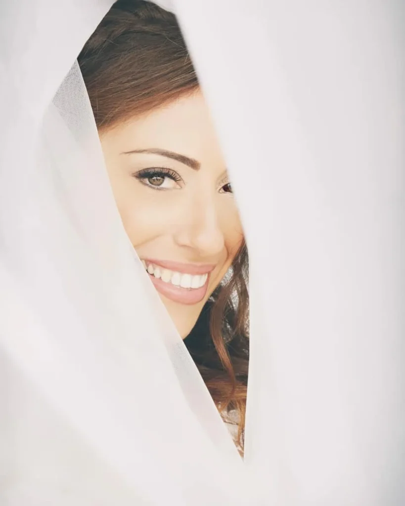 Sposa sorridente incorniciata dal velo con trucco naturale e occhi valorizzati